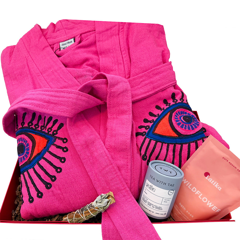 Pink robe with eye design, tea packaging, and bath soak.